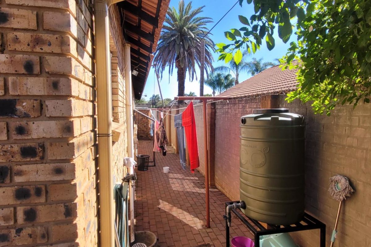A side exterior walkway featuring brick walls, paved flooring, and a fixed water storage tank installation.
