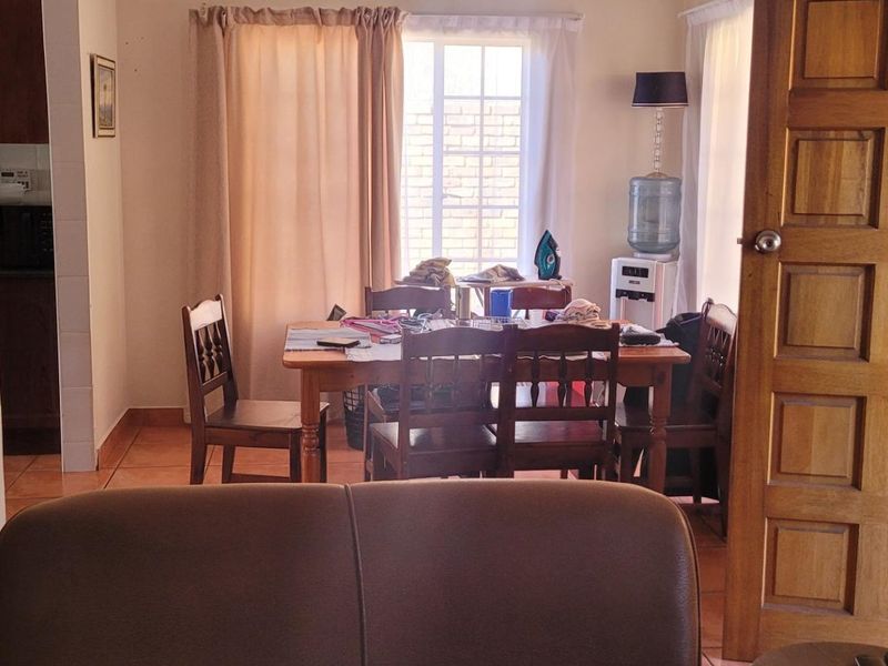 A living area featuring tiled flooring and a traditional wooden panel door, with natural light entering through a window with security bars.
