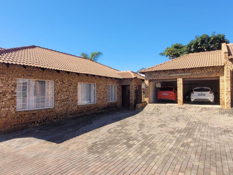 Front view of a face brick house featuring a large paved driveway and multiple garage bays with roller shutter doors.