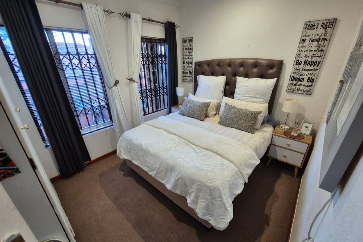 A cozy bedroom featuring carpeted flooring and windows fitted with security gates, providing a functional and secure sleeping space.