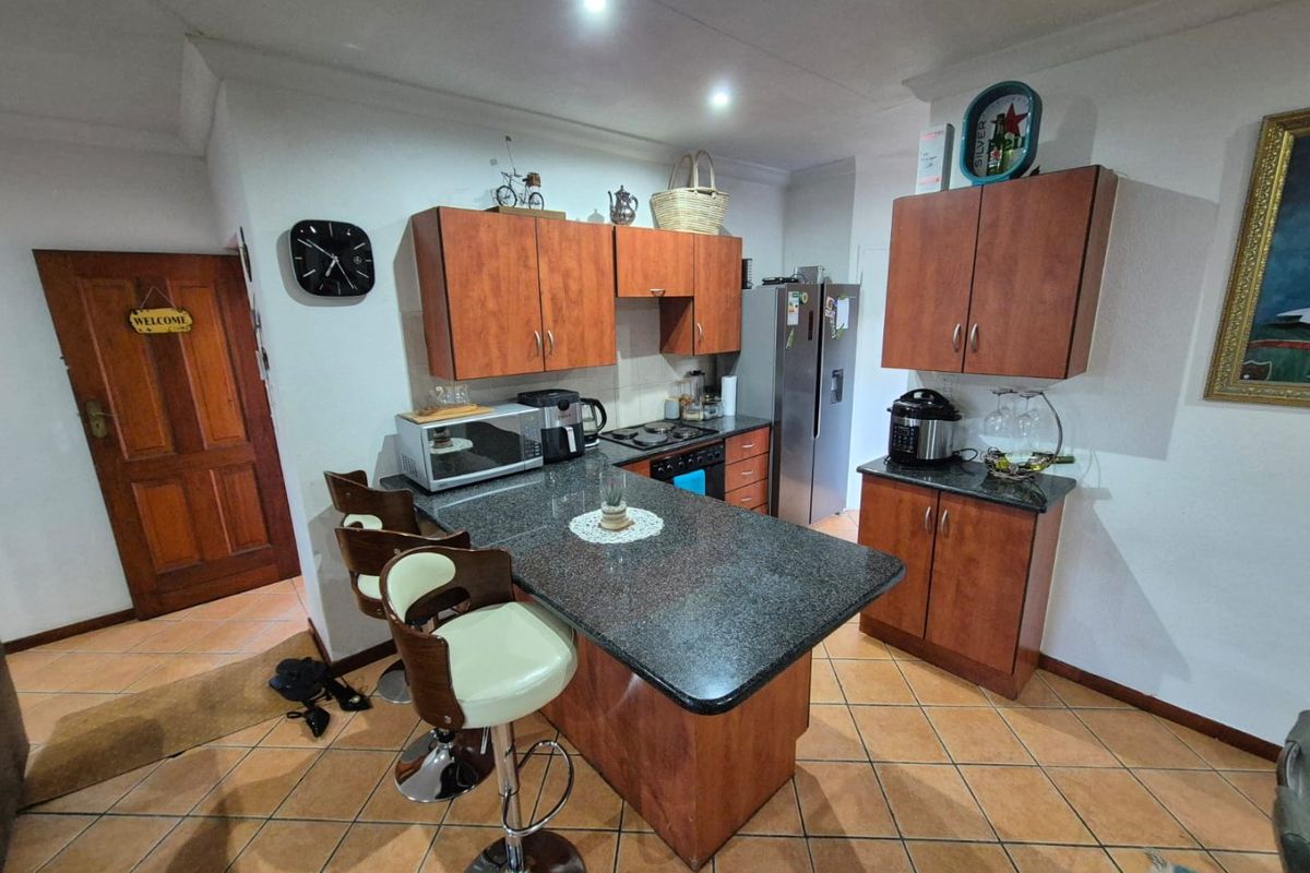 A functional kitchen featuring granite countertops, wooden cabinetry, built-in hob and oven, and tiled flooring with a breakfast bar area.