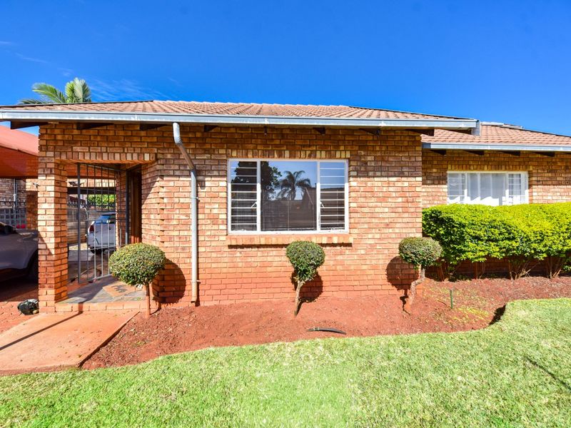 A well-maintained face brick house featuring a tiled roof, secure entrance gate, and a neat front garden with a paved driveway and carport.