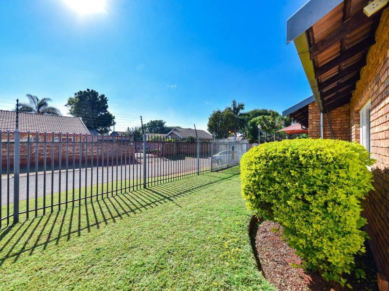 Front exterior view of the property featuring a brick facade, well-maintained lawn, and secure metal perimeter fencing with electric security wires.
