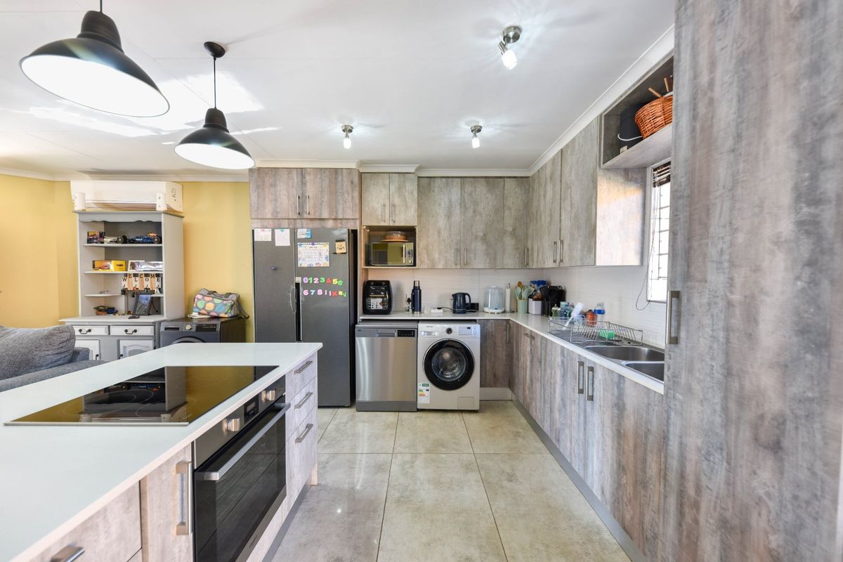 Modern kitchen featuring wood-look cabinetry, a central island with integrated hob and oven, tiled flooring, and ample storage space.
