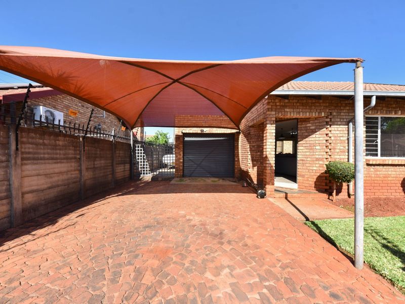 Front exterior view featuring a paved driveway, a large shade sail structure, face brick facade, and a secure garage entrance.