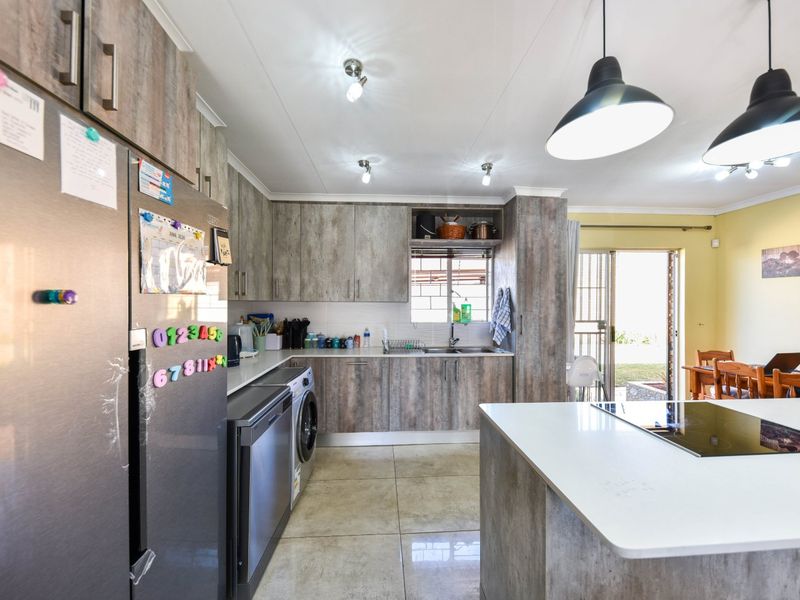 Open plan kitchen featuring modern wood-look cabinetry, a central island with a built-in hob, tiled flooring, and direct access to the outdoor area.