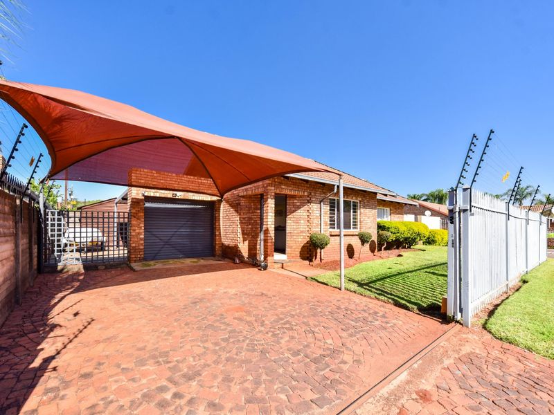 Front exterior view featuring a brick facade, paved driveway, shade sail carport, single garage, and secure electric fencing.