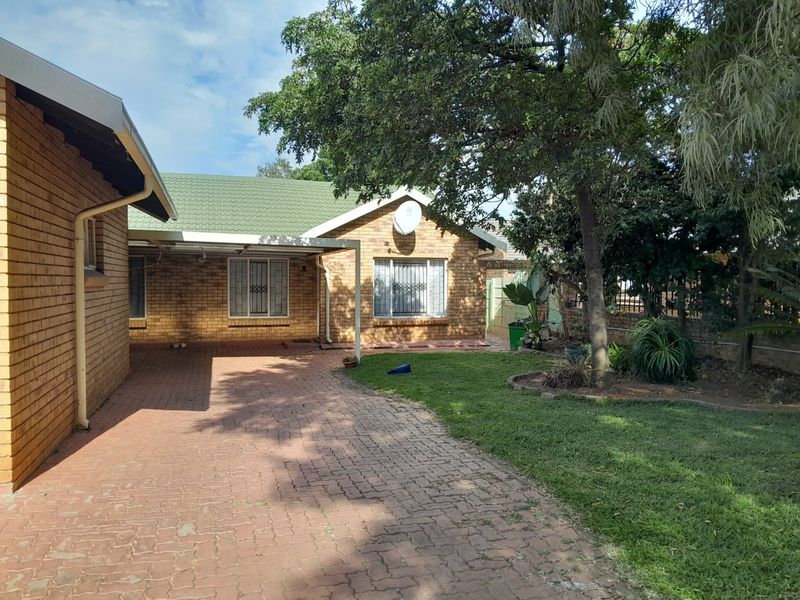 Front view of a brick house featuring a paved driveway, green tiled roof, and established garden area.