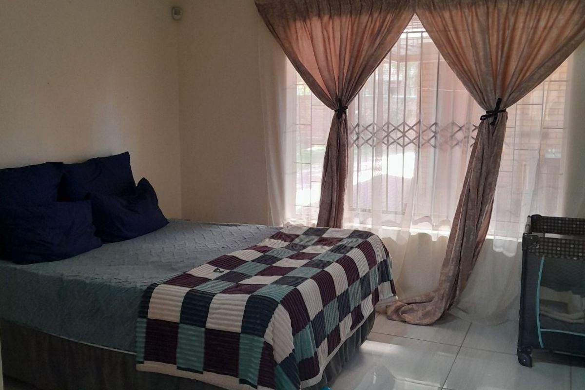A bedroom featuring tiled flooring, a ceiling-mounted spotlight fixture, and a window fitted with a security gate.