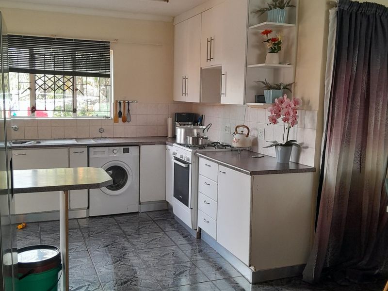 Functional kitchen featuring white cabinetry, laminate countertops, built-in oven with gas hob, and integrated laundry plumbing, finished with tiled flooring and backsplash.