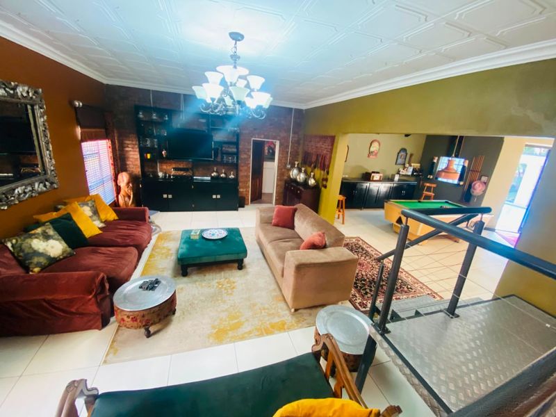 Spacious open-plan living area featuring exposed brick walls, tiled flooring, and a decorative coffered ceiling, with an integrated staircase and adjacent games area.