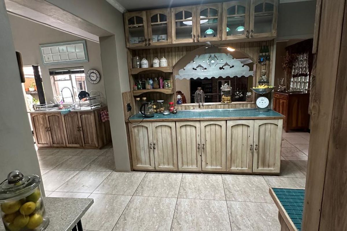 A rustic-style kitchen featuring extensive built-in wooden cabinetry, tiled countertops, and large floor tiles, with an open-plan layout connecting to an adjacent prep area.