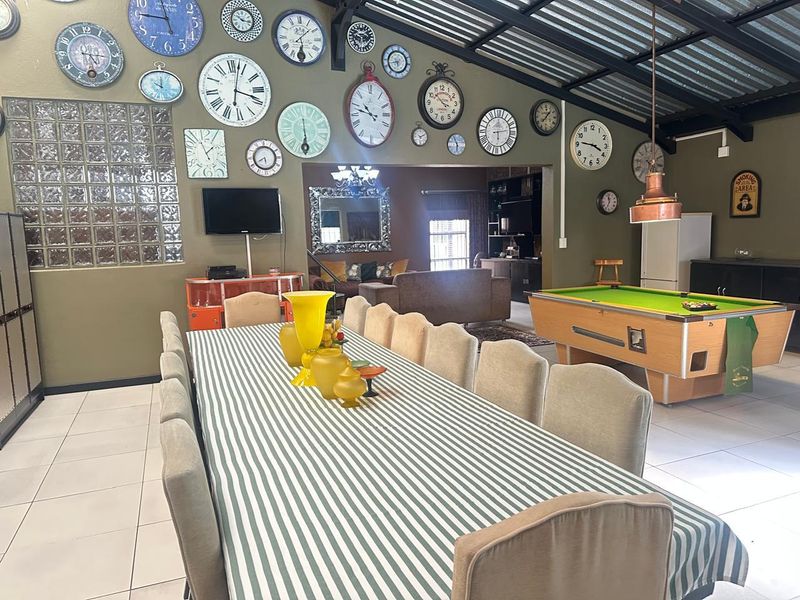 Spacious open-plan living and dining area featuring exposed steel roof trusses, glass block feature wall, and tiled flooring, offering a versatile entertainment space.