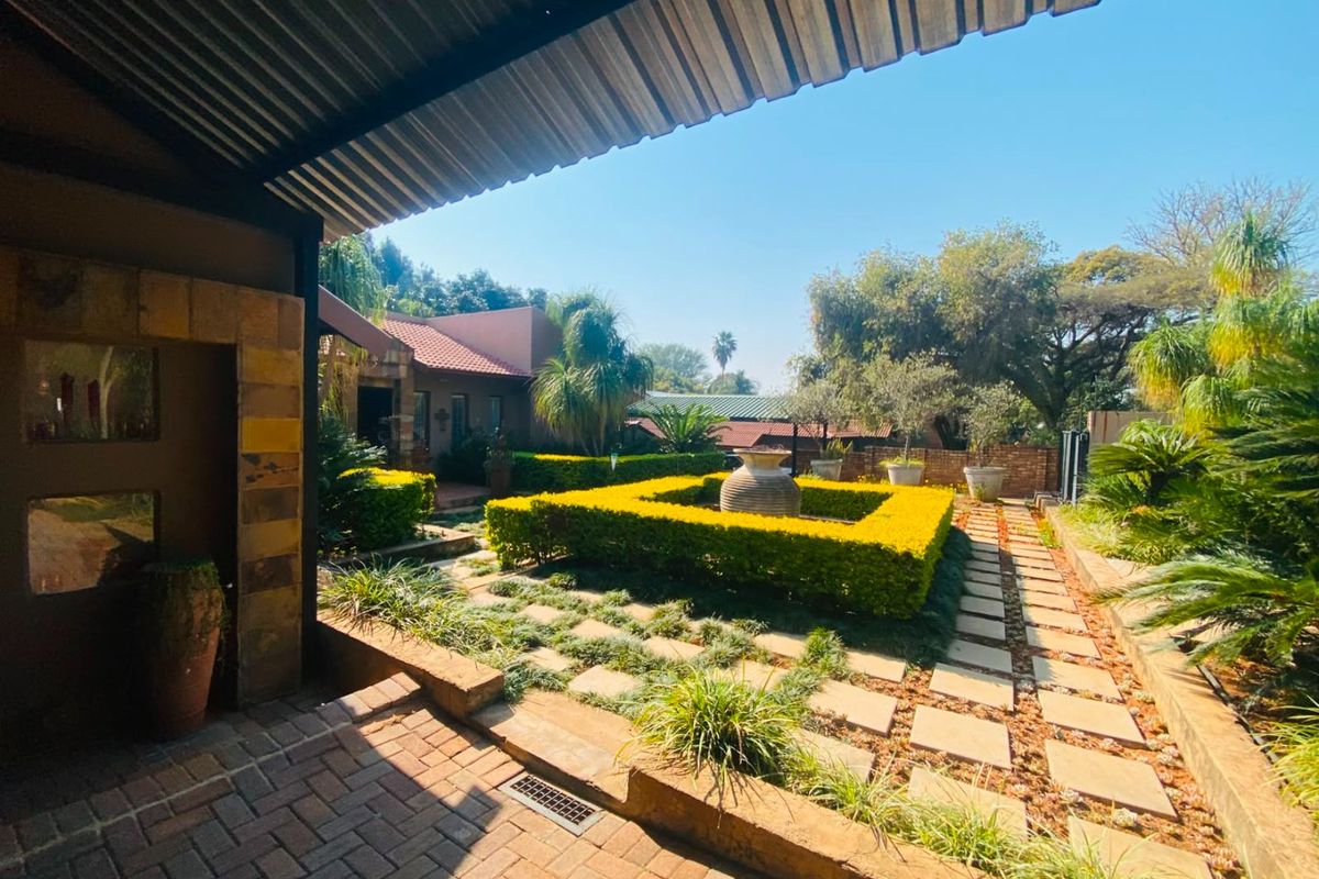 A well-maintained rear garden featuring a paved patio area, structured hedging, and stone-clad architectural details under a covered outdoor space.