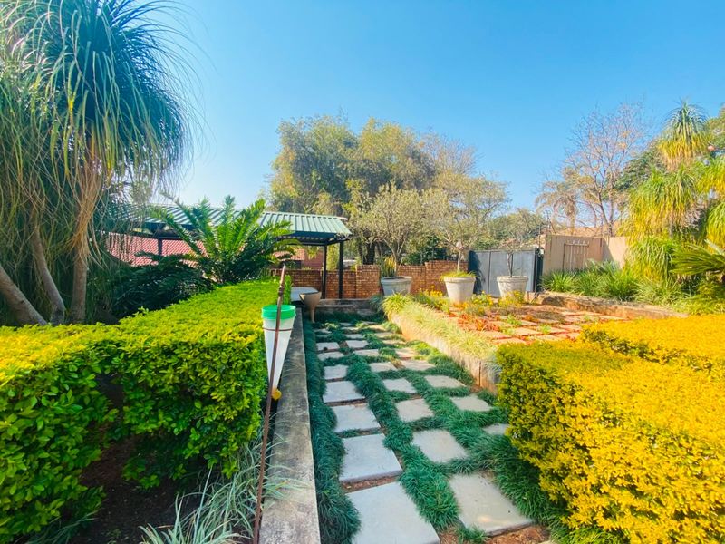 A well-maintained garden featuring a stone paver pathway, manicured hedges, and a covered patio area in the background.