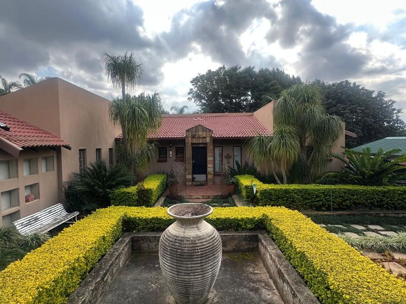 Front elevation of a house featuring a central ornamental water feature, manicured hedges, and a terracotta tiled roof with stone facade detailing.