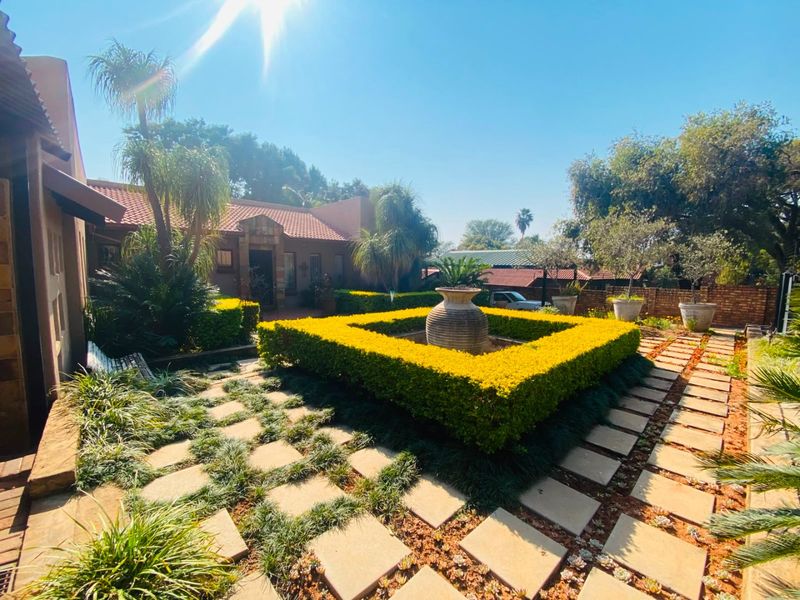 A well-maintained front garden featuring a central stone fountain, manicured hedges, and a paved walkway leading to the main house entrance.