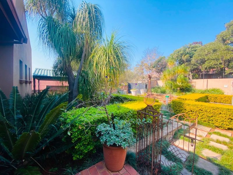 A well-maintained private garden featuring mature trees, manicured hedges, and a paved walkway leading through the landscaped outdoor space.