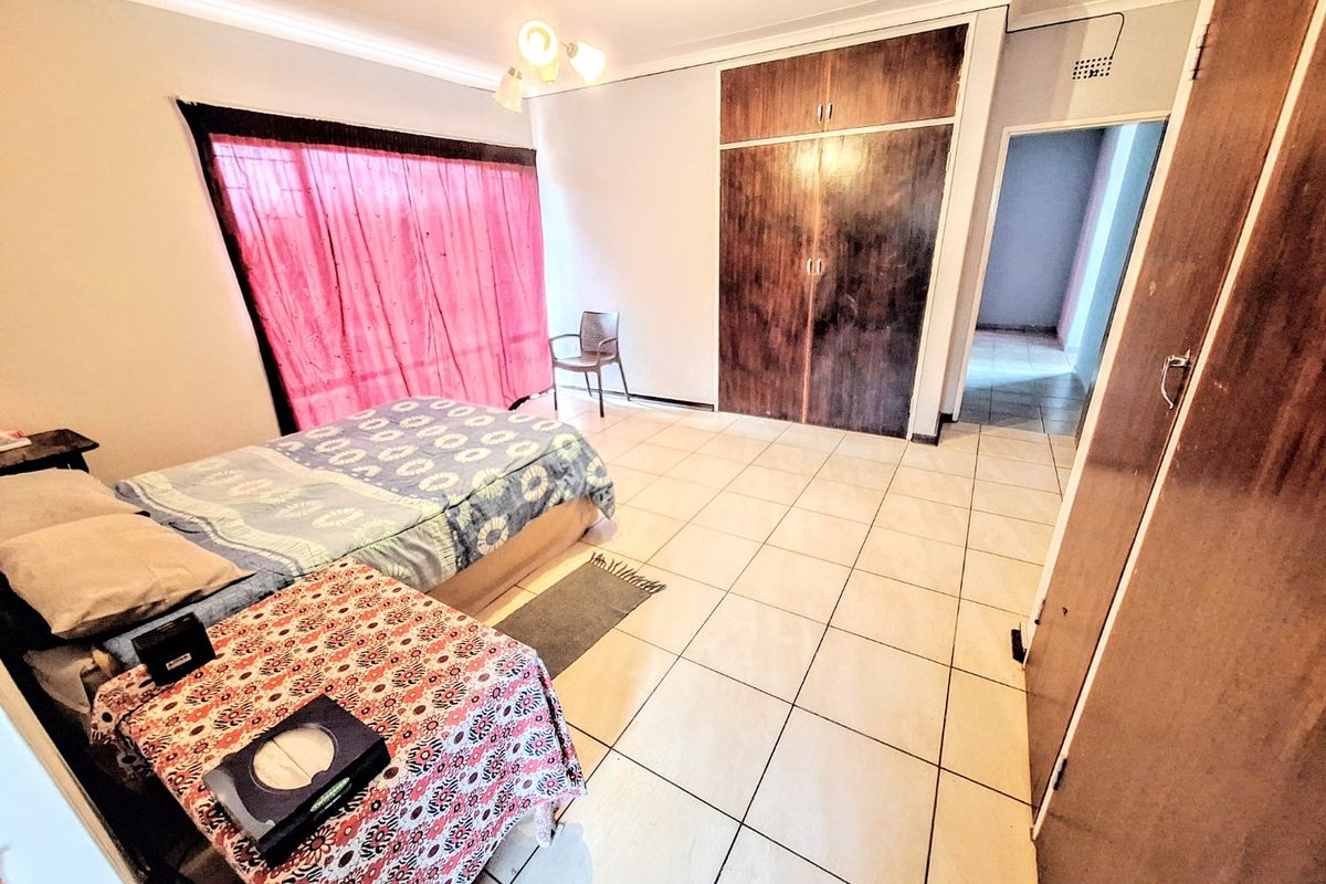 A spacious bedroom featuring tiled flooring and built-in wooden cupboards, offering a functional layout with natural light through the window.
