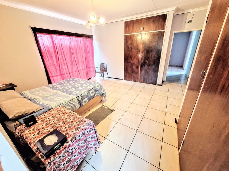 A spacious bedroom featuring tiled flooring and built-in wooden cupboards, offering a functional layout with natural light through the window.