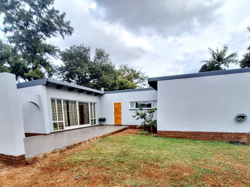 Rear view of the house featuring a tiled patio, sliding glass doors, and a well-maintained exterior with a brick base and lawn area.