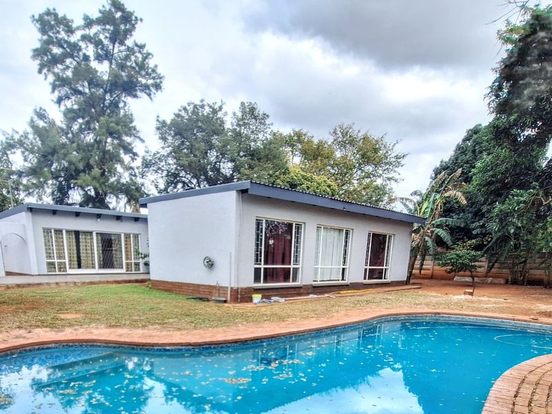 Rear view of the property featuring a swimming pool with brick coping, large windows with security bars, and a spacious garden area.