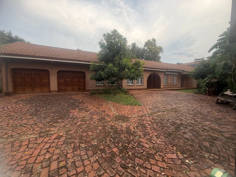 Front elevation of a single-story house featuring a double garage, arched wooden entrance, and a large cobblestone driveway.