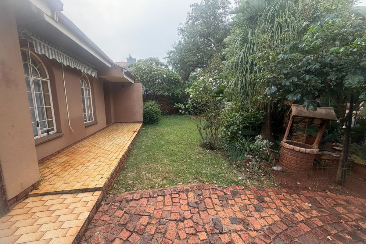 Rear garden area featuring a tiled patio with a retractable awning, brick paving, and a decorative brick well feature.