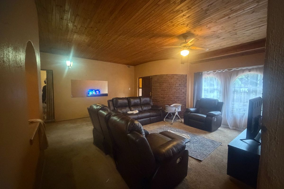 Spacious living room featuring a warm timber tongue and groove ceiling, an exposed brick feature wall, and arched windows.