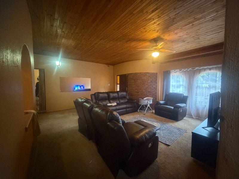 Spacious living room featuring a warm timber tongue and groove ceiling, an exposed brick feature wall, and arched windows.
