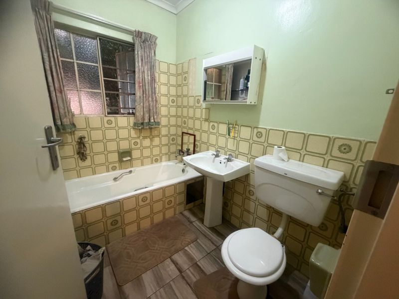 A dated bathroom featuring a bathtub, pedestal basin, and toilet with original patterned wall tiles and a medicine cabinet.