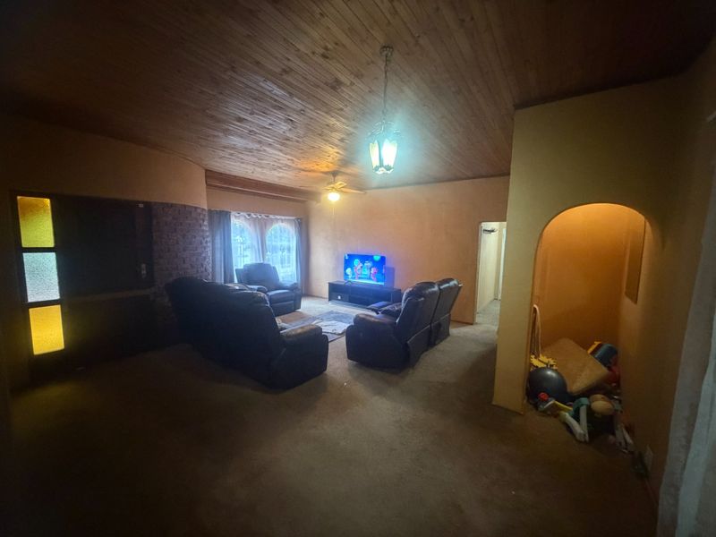 Spacious living room featuring a timber-clad vaulted ceiling, exposed brick accent wall, and an arched entryway, offering a rustic aesthetic with potential for modernization.