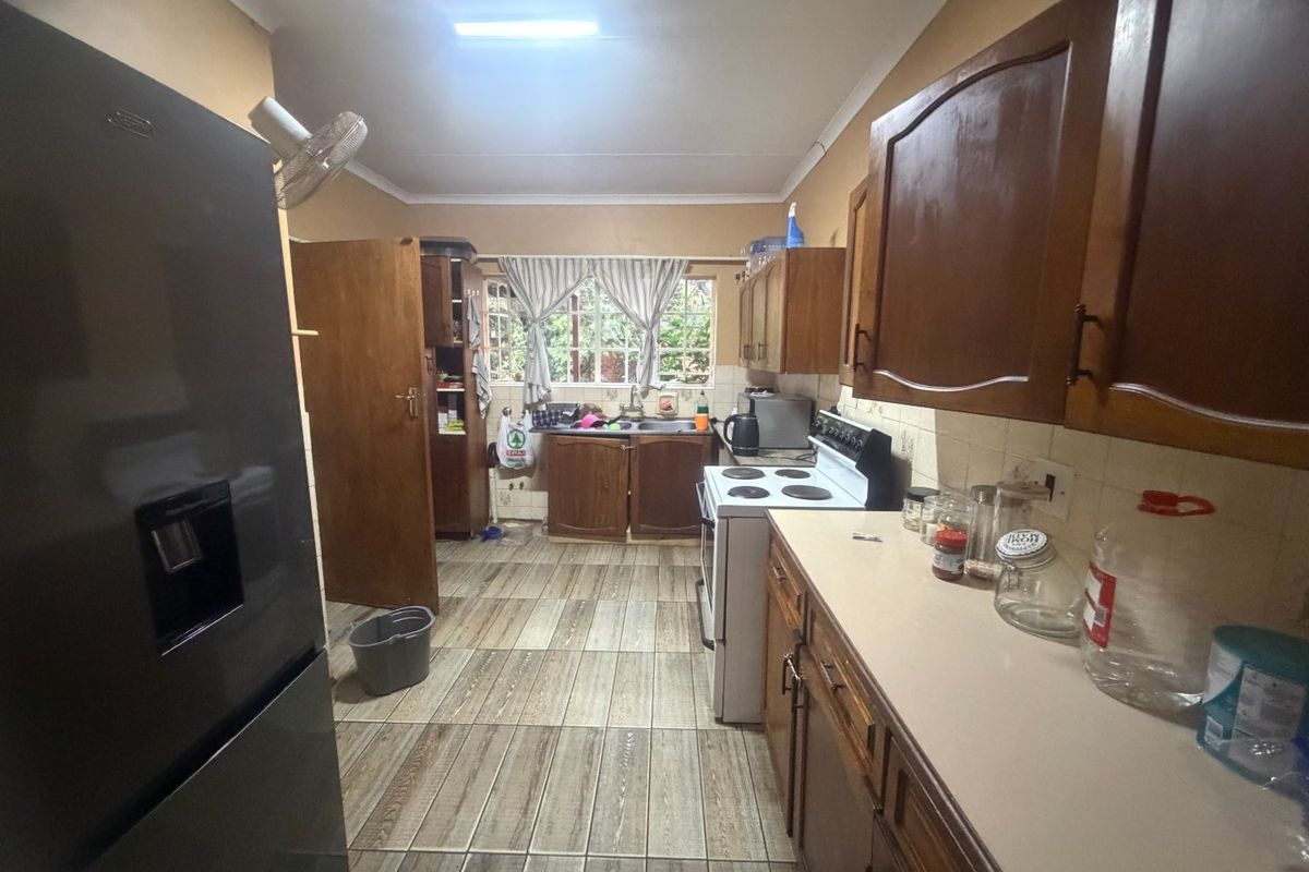 A functional kitchen featuring wooden cabinetry, laminate countertops, a double basin sink, and tiled flooring, offering potential for a modern renovation.