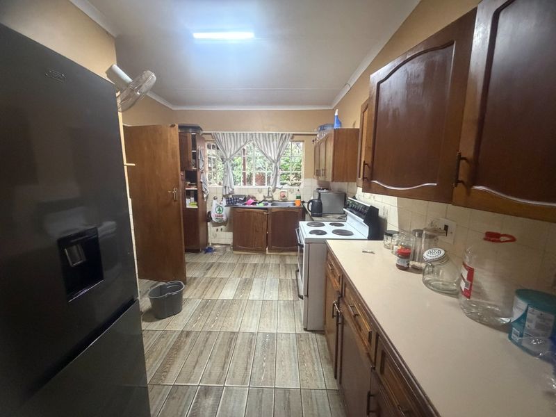 A functional kitchen featuring wooden cabinetry, laminate countertops, a double basin sink, and tiled flooring, offering potential for a modern renovation.