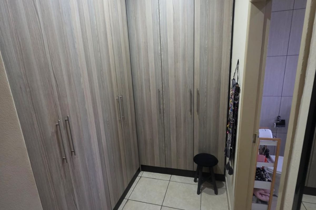 A clean dressing area featuring extensive floor-to-ceiling built-in cupboards with wood-grain finish and neutral tiled flooring.