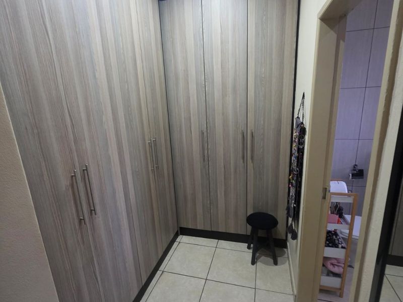 A clean dressing area featuring extensive floor-to-ceiling built-in cupboards with wood-grain finish and neutral tiled flooring.