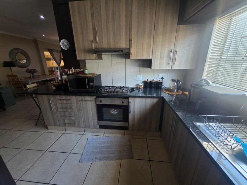 A functional kitchen featuring wood-look cabinetry, granite countertops, a gas hob, built-in oven, and tiled flooring, with an adjacent dining area visible.