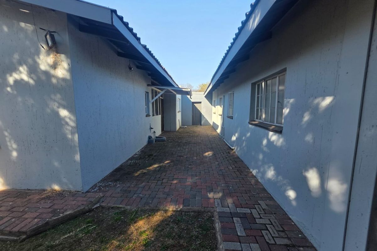 A narrow paved walkway between two sections of the house, featuring brick paving and steel-framed windows.