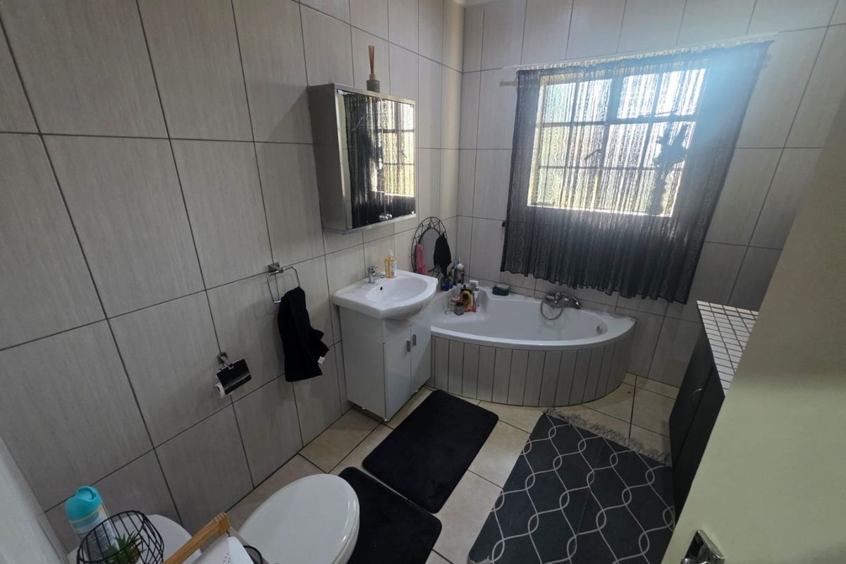 A functional bathroom featuring a corner bathtub, vanity basin, toilet, and full-height wall tiling.