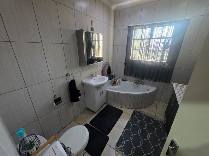 A functional bathroom featuring a corner bathtub, vanity basin, toilet, and full-height wall tiling.
