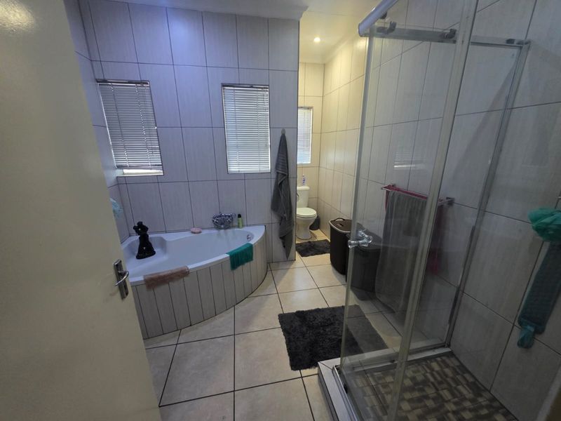 A functional bathroom featuring a corner bathtub, a separate glass-enclosed shower, and a toilet, finished with neutral wall and floor tiling.