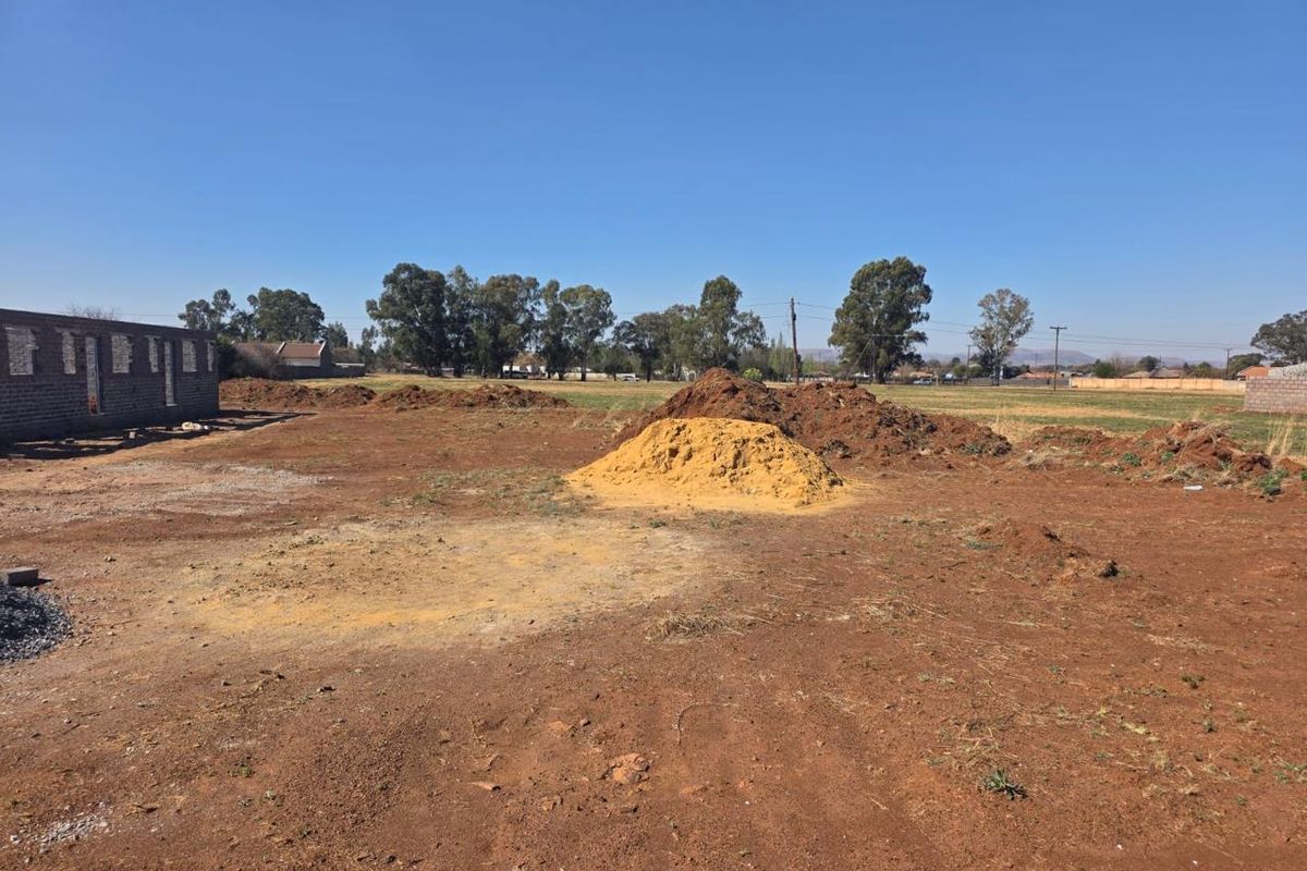 A large, undeveloped plot of land featuring an unfinished masonry structure and piles of excavated soil, offering significant potential for custom development.