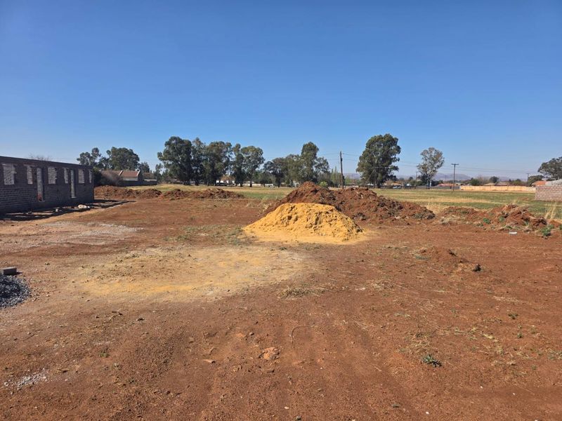 A large, undeveloped plot of land featuring an unfinished masonry structure and piles of excavated soil, offering significant potential for custom development.
