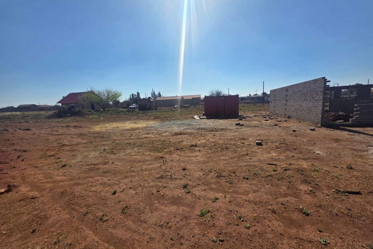 A large, undeveloped plot of land featuring an unfinished boundary wall and open space, offering significant potential for future development or landscaping.