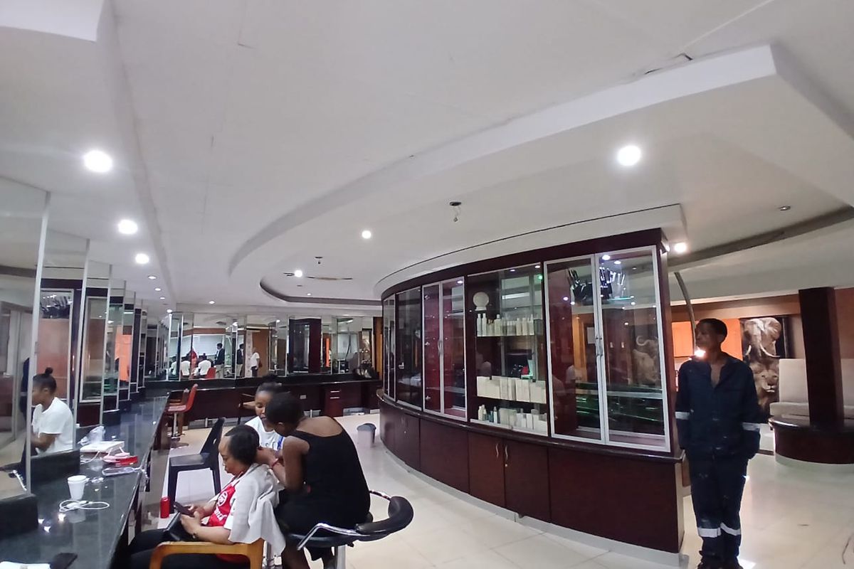 A commercial salon space featuring curved built-in display cabinetry, extensive wall-mounted mirrors, and integrated recessed ceiling lighting.