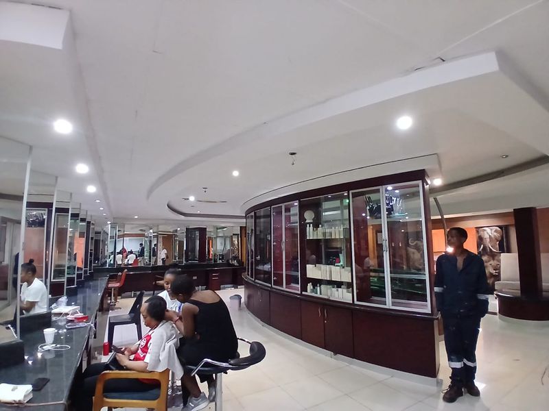 A commercial salon space featuring curved built-in display cabinetry, extensive wall-mounted mirrors, and integrated recessed ceiling lighting.