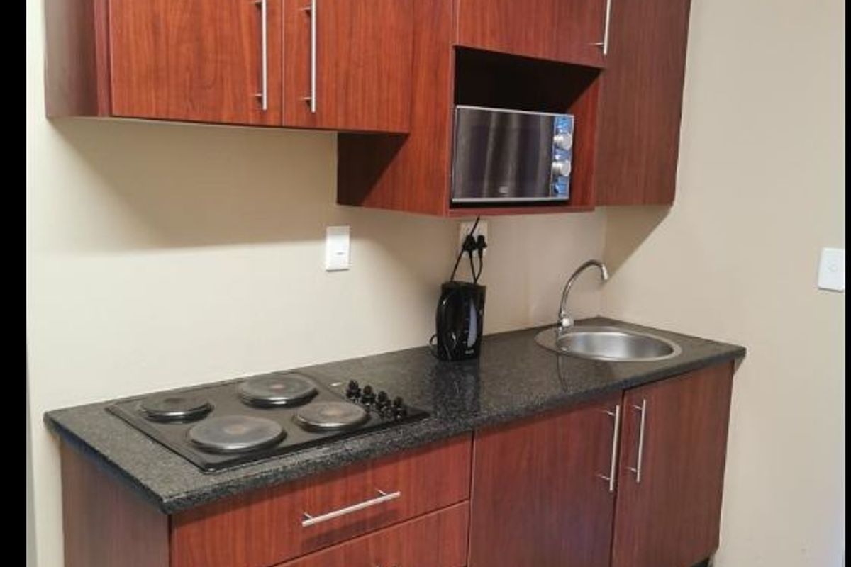 Compact kitchen featuring dark wood cabinetry, granite countertops, an integrated electric hob, built-in microwave, and a stainless steel sink.