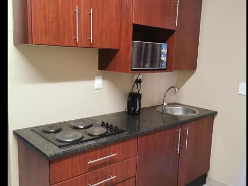 Compact kitchen featuring dark wood cabinetry, granite countertops, an integrated electric hob, built-in microwave, and a stainless steel sink.