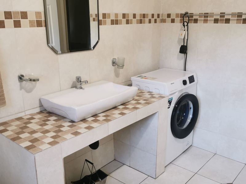 A functional laundry area featuring a tiled vanity with a vessel sink, ceramic wall and floor tiling, and space for a washing machine.