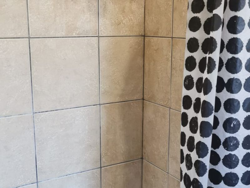 A shower enclosure featuring beige ceramic wall and floor tiles with a standard shower head fixture.